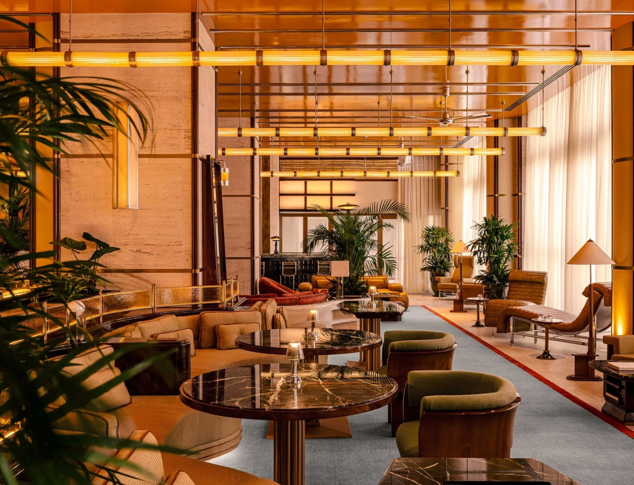 Orient Express Dolce Vita lounge with marble tables, curved sofas and warm brass lighting in an elegant, plant-filled room 