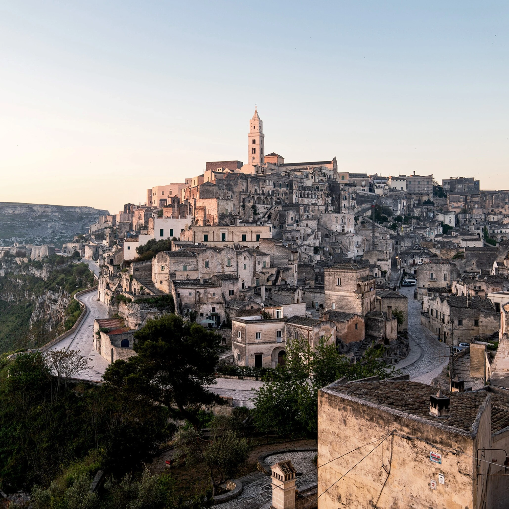 Matera's ancient stone houses cascading down the Sassi cliffs at sunrise, historic cathedral tower above 